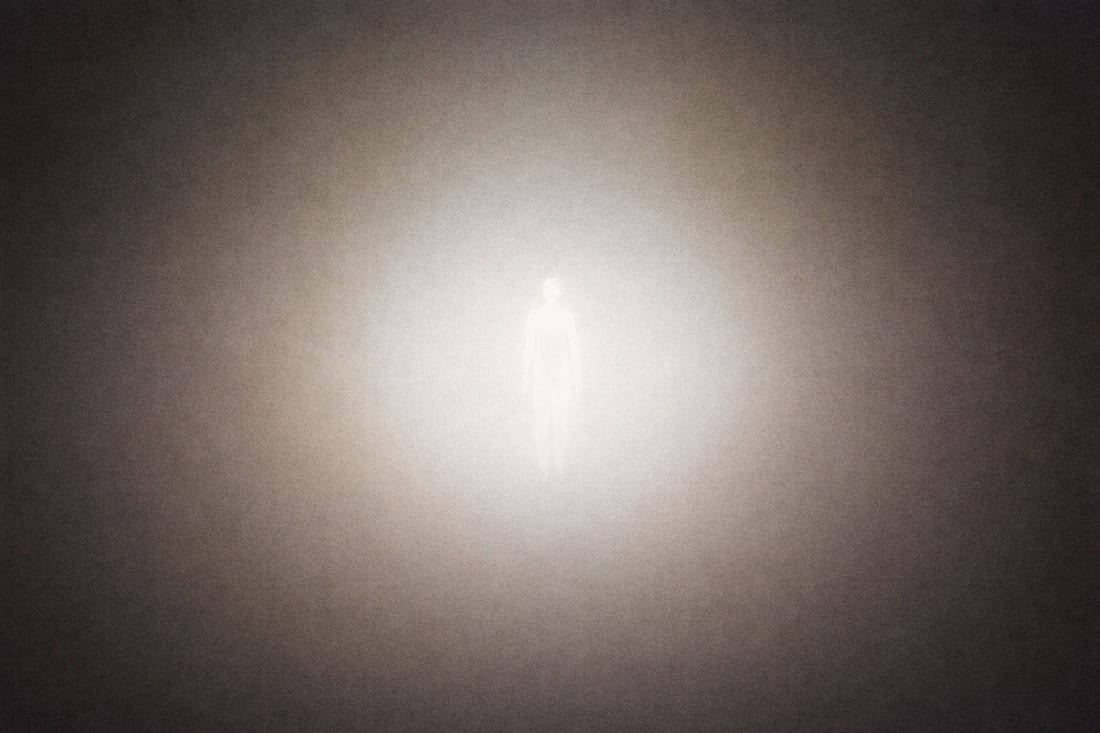 A glowing human-like silhouette stands in the center of a hazy, light-filled space, surrounded by soft gradients of grey and gold light that fade into darkness.