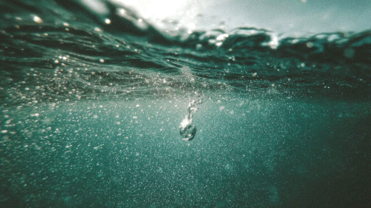 A macro photograph of a single water droplet hitting a calm surface, creating perfect concentric ripples that symbolize the expansion of Divine Light (Noor).