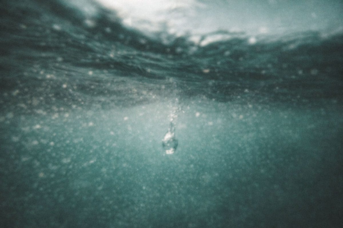 A macro photo of a single water droplet hitting a calm surface, creating perfect concentric ripples that symbolize the expansion of Divine Light. | Teachings from Khawaja Shamsuddin Azeemi.